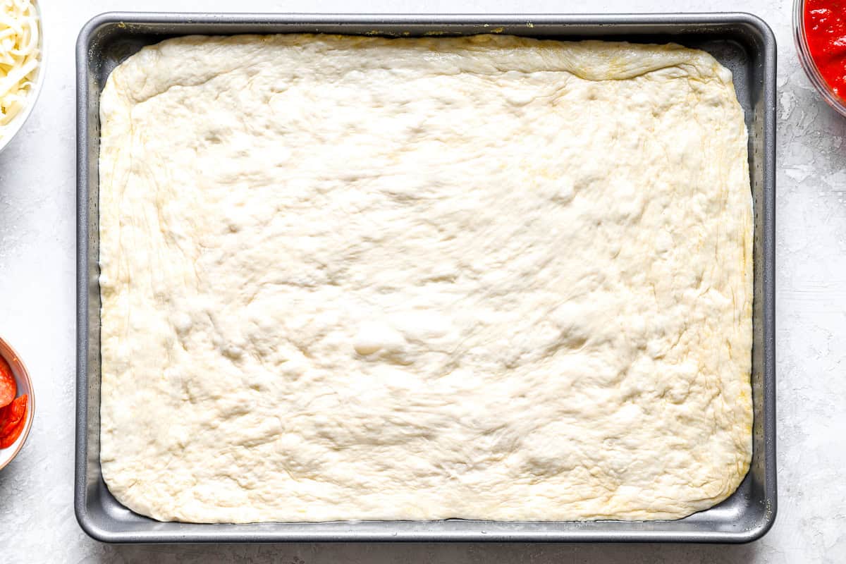 Raw pizza dough stretched and pressed into the corners of an oiled sheet pan
