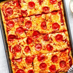Overhead shot of sliced pepperoni sheet pan pizza in a metal pan, golden crust visible around the edges
