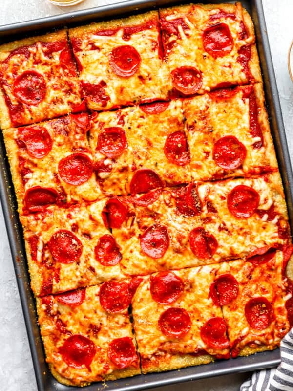 Overhead shot of sliced pepperoni sheet pan pizza in a metal pan, golden crust visible around the edges
