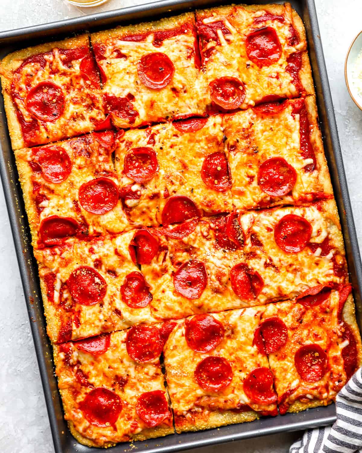 Overhead shot of sliced pepperoni sheet pan pizza in a metal pan, golden crust visible around the edges