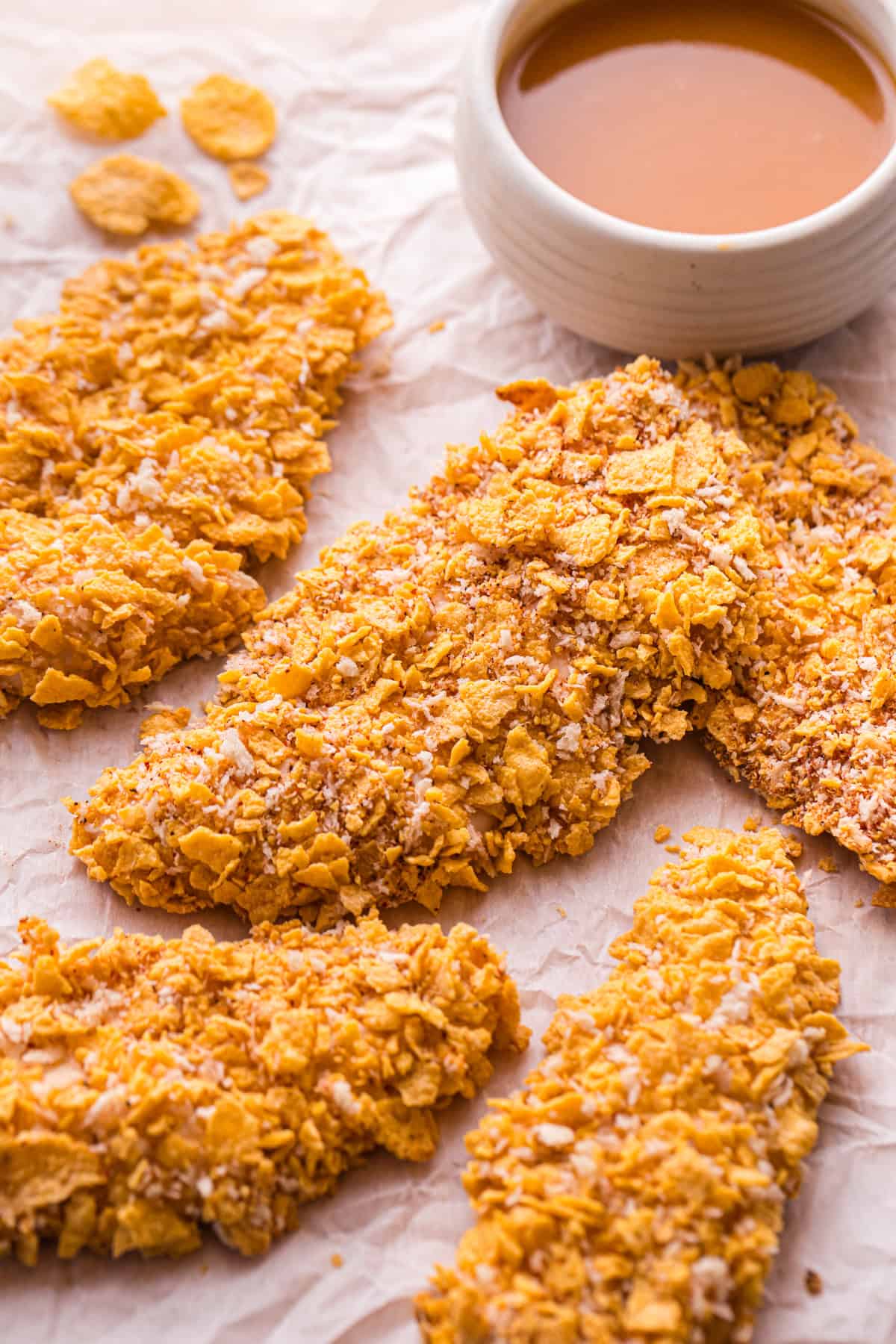 Crispy cornflake buffalo chicken tenders arranged next to a bowl of brown butter buffalo sauce