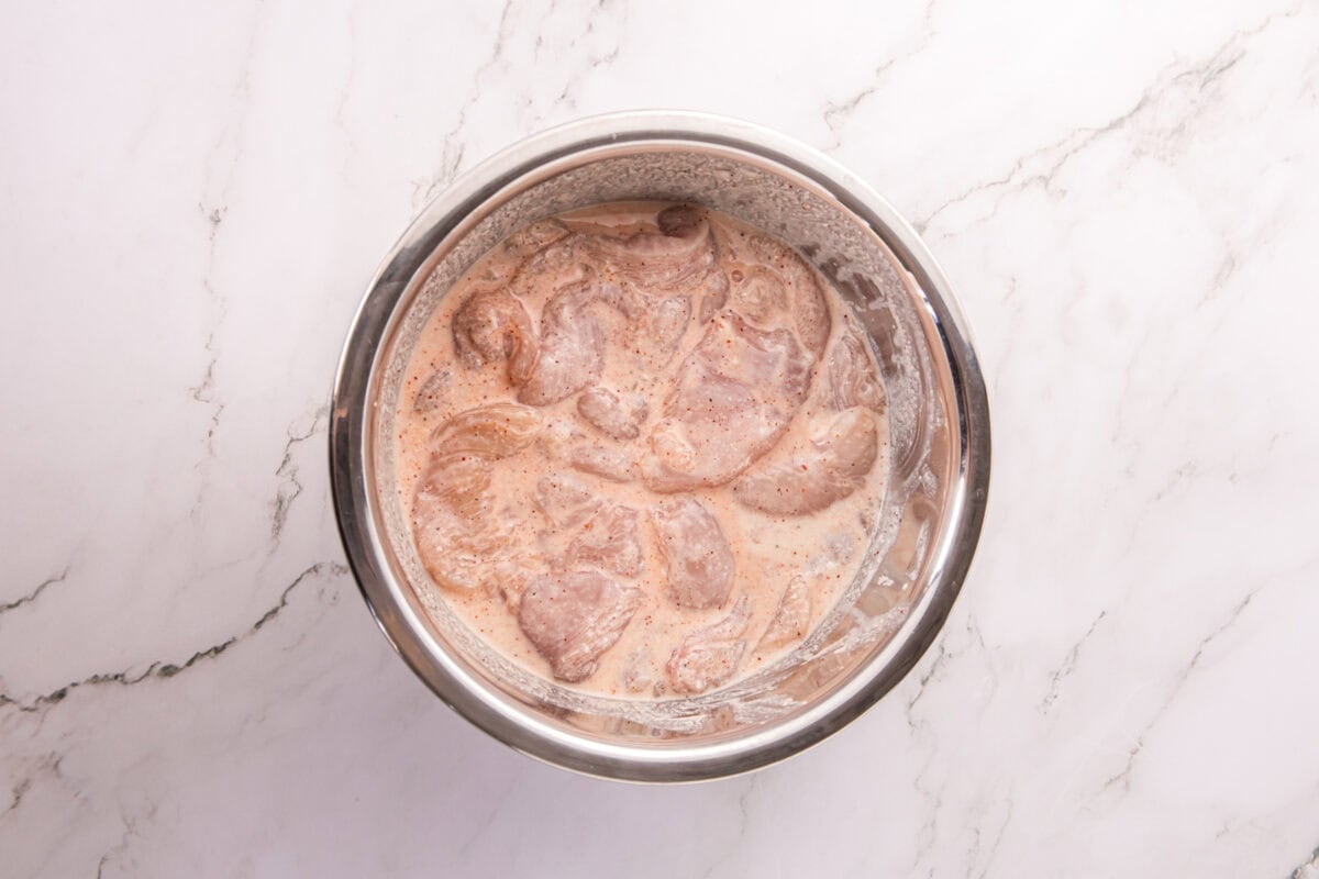 Chicken tenderloins soaking in a buttermilk marinade in a metal mixing bowl