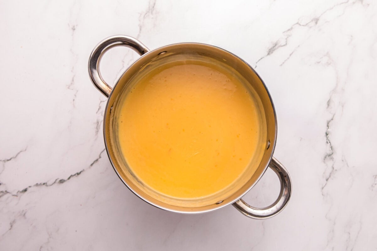Smooth, glossy melted cheese sauce in a saucepan, ready to pour over the fries.