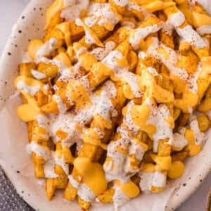 Louisiana Voodoo Fries on a plate, loaded with warm cheese sauce, cool ranch, and a sprinkle of Cajun seasoning.
