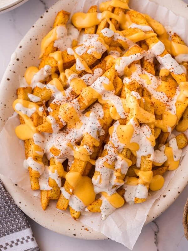 Louisiana Voodoo Fries on a plate, loaded with warm cheese sauce, cool ranch, and a sprinkle of Cajun seasoning.