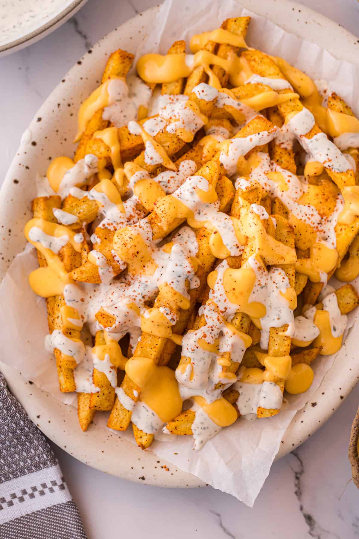 Louisiana Voodoo Fries on a plate, loaded with warm cheese sauce, cool ranch, and a sprinkle of Cajun seasoning.