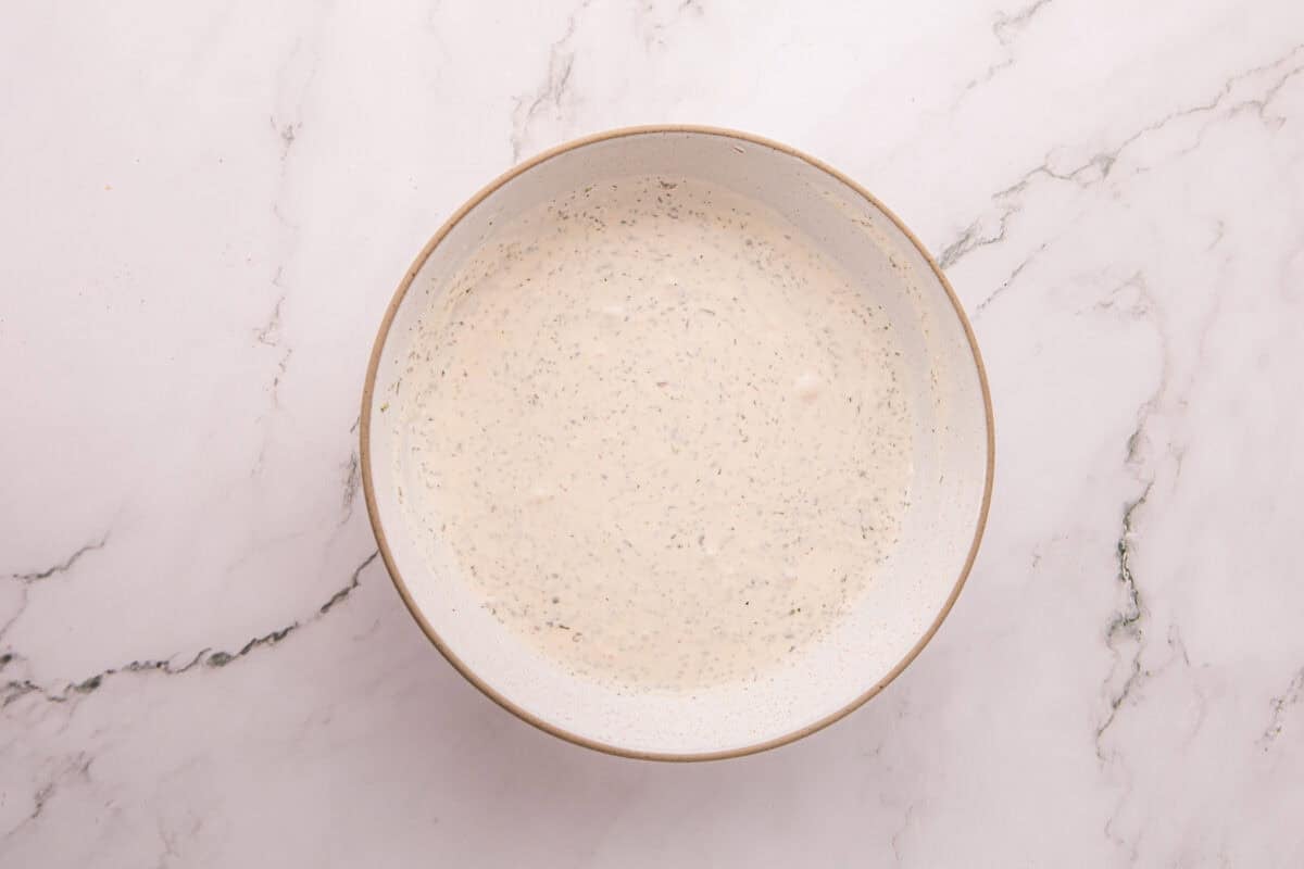 Homemade ranch dressing mixed in a bowl, flecked with dill and parsley.