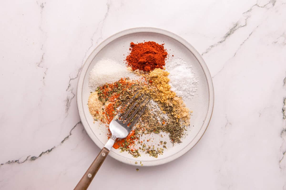Cajun seasoning spices measured out on a plate before being mixed together with a fork.