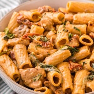 Close-up of creamy Tuscan chicken pasta in a bowl, showing rigatoni, spinach, and sun-dried tomatoes coated in Parmesan cream sauce.