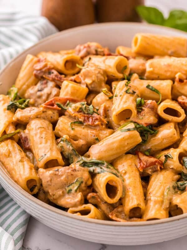 Close-up of creamy Tuscan chicken pasta in a bowl, showing rigatoni, spinach, and sun-dried tomatoes coated in Parmesan cream sauce.