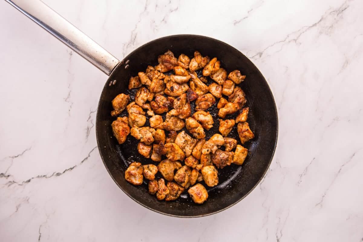 Golden seared chicken pieces cooking in a black skillet.