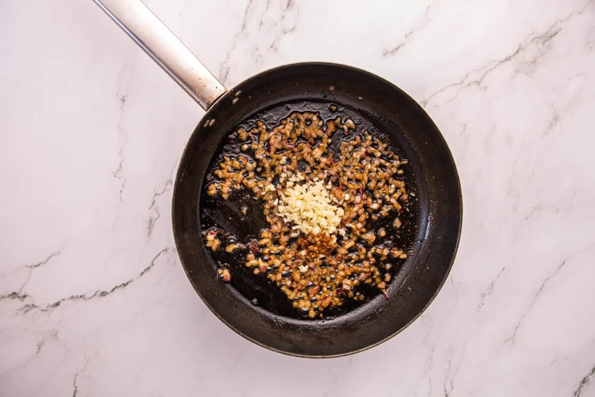 Chopped shallot, minced garlic, and red pepper flakes sautéing in a skillet.