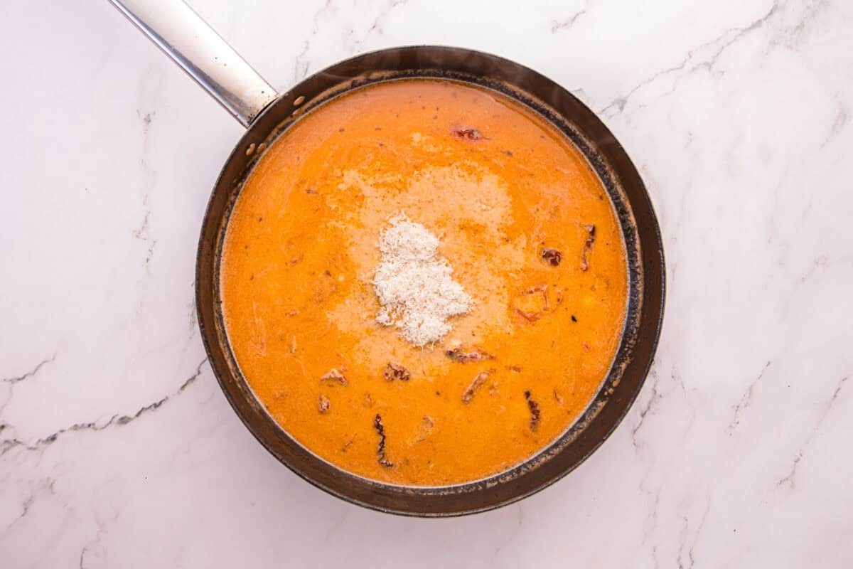 Freshly grated Parmesan added to the creamy Tuscan sauce in a skillet.