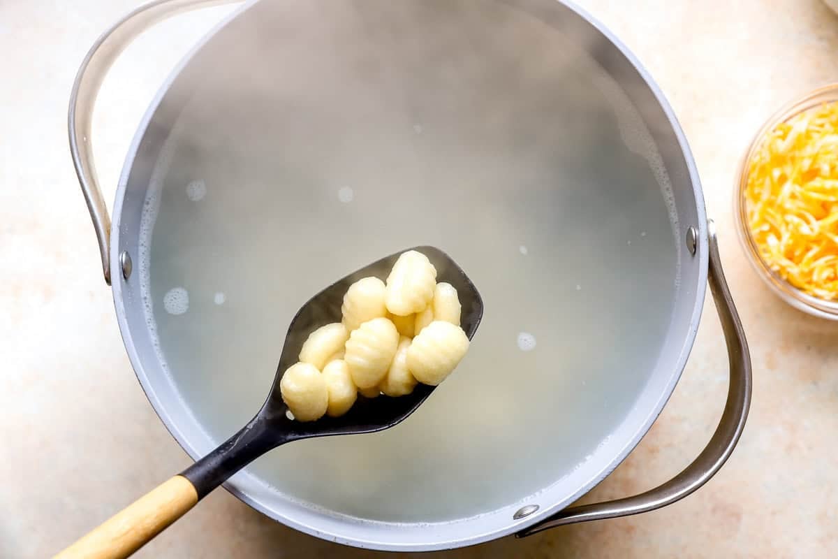 Slotted spoon lifting cooked gnocchi out of a pot of boiling water.