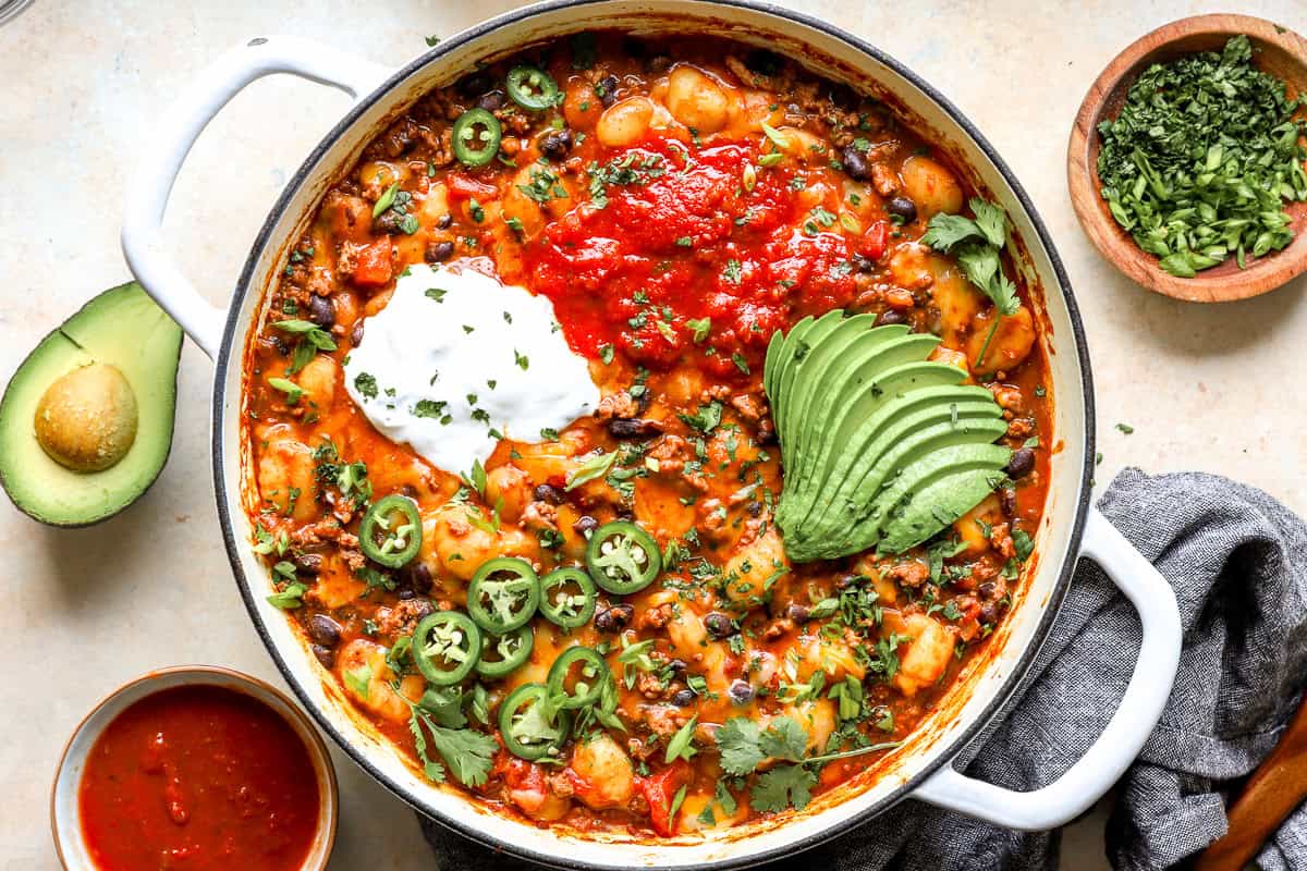 Overhead shot of the finished taco gnocchi skillet topped with sour cream, salsa, avocado, jalapeños, and cilantro.